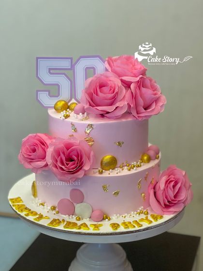 A beautiful two-tier cake for a 50th birthday celebration. The pink ombre design is decorated with fresh pink roses and gold leaf for an elegant and celebratory look.