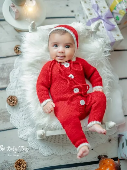 A full-length portrait of a newborn in a tiny bed, dressed as Santa's little helper. The surrounding presents and pinecones complete the festive scene.