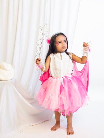 A child model dressed as a pink fairy, complete with a tutu, wings, and a star wand.