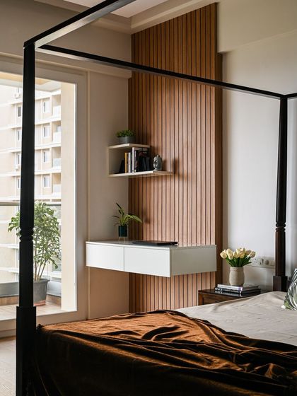 This bedroom features a classic four-poster bed, which adds a touch of timeless elegance. Adjacent to it, a floating white console table is set against a wooden fluted wall, creating a functional and stylish study nook.