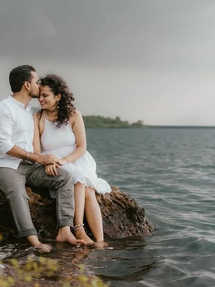 A tender moment between a couple sitting by the water's edge, with moody skies overhead. This captures a quiet, intimate connection.