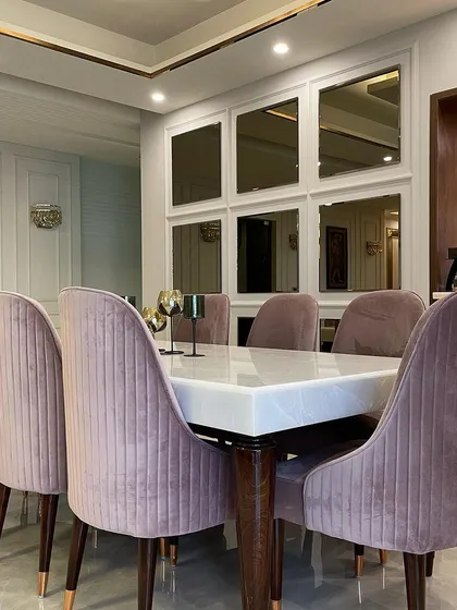 The dining chairs are upholstered in a dusty rose velvet with vertical tufting, complementing the living room furniture. The solid white marble tabletop provides a clean, bright surface.