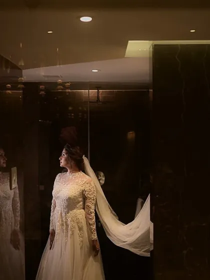 A dramatic and beautiful shot of the bride with her veil. The lighting creates a stunning silhouette, highlighting her elegant gown and hairstyle.