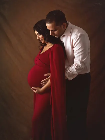 A classic and intimate portrait in a bold red gown. The dark, moody lighting and the husband's gentle embrace from behind create a powerful and romantic image focused on the couple's connection.