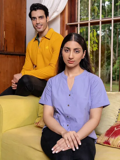 An indoor lifestyle shot for MG Motor's apparel line. The models are posed on a couch, creating a comfortable, at-home scene that showcases the versatility of the clothing.
