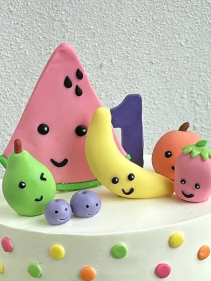 A close-up of the topper for the fruits-themed cake, featuring a fondant watermelon, banana, and other smiling fruits.