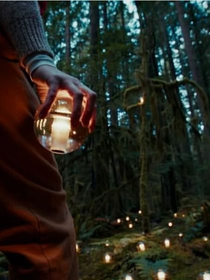 The portable Bocci 14p lamp is held in hand during a walk through a forest, its warm glow lighting the path. This image beautifully illustrates the lamp's purpose: to bring a sphere of personal, ambient light wherever you go.