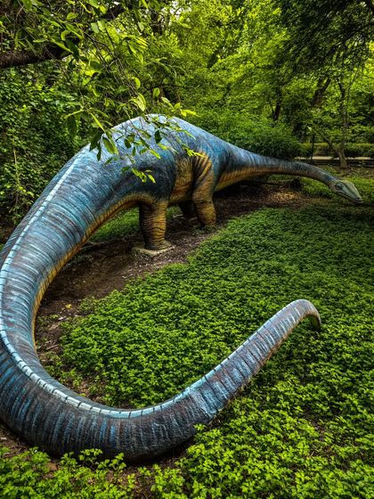 A different angle of the dinosaur statue, showing its long neck and tail amidst the lush greenery.