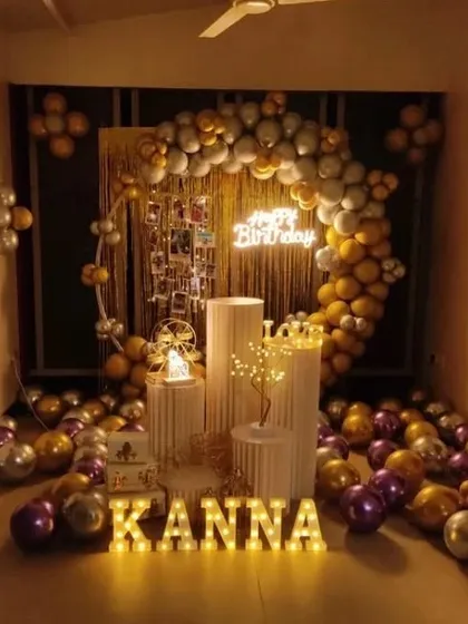 A warm and inviting birthday setup for Kanna. A gold, silver, and purple balloon arch is combined with a photo display, neon sign, and illuminated letters for a personalized touch.
