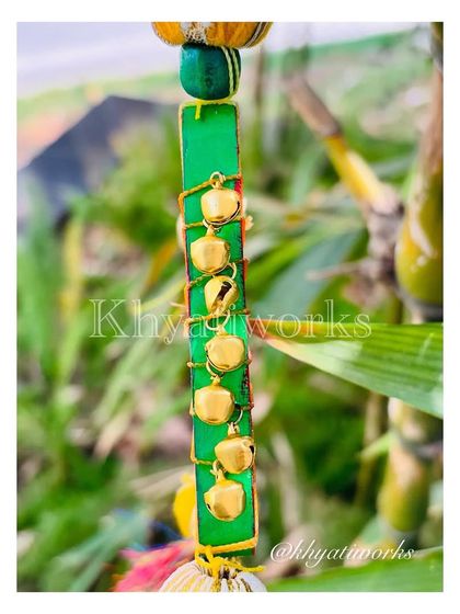 A close-up of the side of the kite hanging, wrapped in green with tiny golden bells that jingle softly.