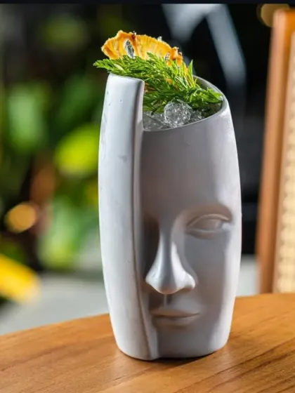 We use unique and artistic glassware to make our drinks stand out. This tiki-style cocktail is served in a face-shaped ceramic mug, adding to the exotic experience.