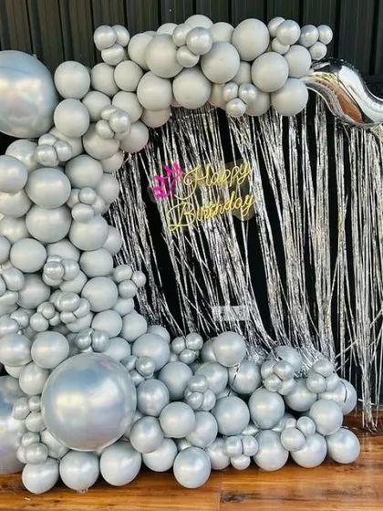 A modern birthday setup with a silver fringe curtain. The decoration features a full silver balloon garland, creating a sleek, monochromatic look.
