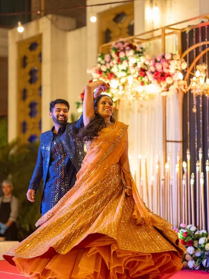 A candid moment of the couple dancing at their Sangeet. The warm lighting and floral backdrop create a romantic and celebratory atmosphere for their performance.