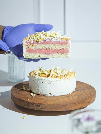 A slice of our Vanilla Raspberry ice cream cake held aloft, showcasing the beautiful pink and white layers. This is what pure, handcrafted goodness looks like.