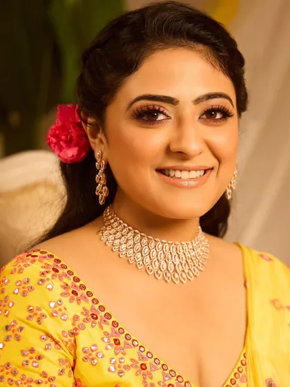 This half-up, half-down hairstyle for a Haldi ceremony is both beautiful and practical. It features a braided crown and soft waves, decorated with baby's breath and a single bright flower for a pop of color.