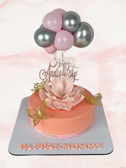 A fun and whimsical anniversary cake for "Pappa & Mummy". The design features a cascade of pink and silver balloons, a beautiful sugar flower, and delicate golden butterflies.