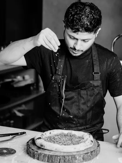 Chef Sudeep at work, adding a final sprinkle of seasoning to a pizza before it goes into the oven.