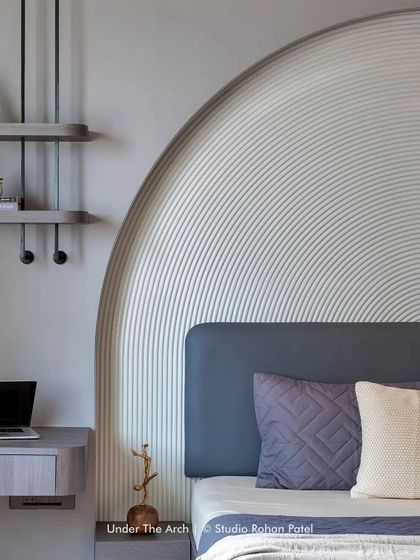 The bedroom continues the theme of arches with a large, fluted arch forming the headboard, creating a soft and sculptural backdrop.