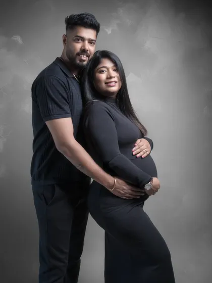 A classic and elegant couple portrait. Dressed in black against a textured grey backdrop, their pose is confident and connected. This is a timeless image celebrating their journey to parenthood.