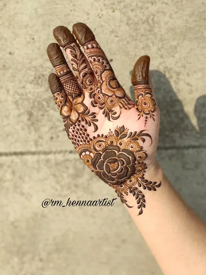 An Eid henna inspiration with a beautiful rose at the base of the palm. The fingers are decorated with delicate floral and leafy patterns.