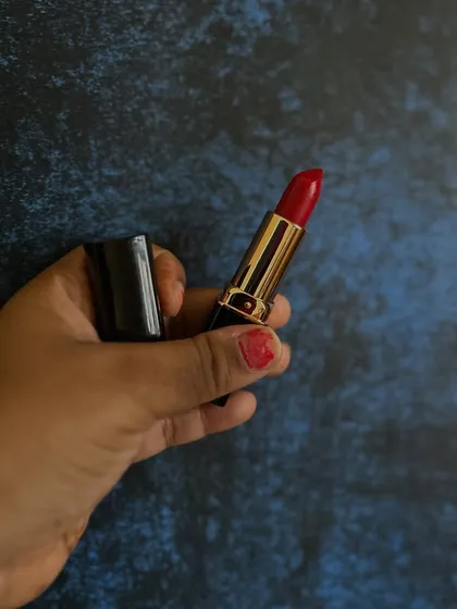 Holding up my handmade lipstick in a classic red shade. The gold and black packaging feels luxurious, but the formula inside is all-natural.