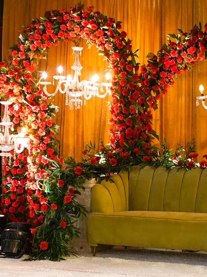 A close-up of a unique seating arrangement, featuring a green velvet sofa framed by arches of red roses and elegant chandeliers. This creates a luxurious and intimate photo spot.
