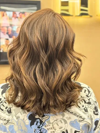 The back of a client's hair, showing a beautiful color blend styled into soft waves. The look is fresh, modern, and full of dimension.