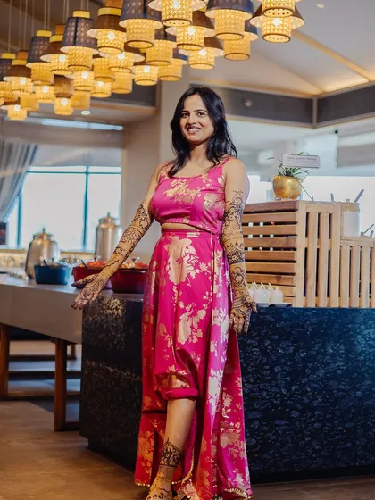 A full-length portrait of the bride in her modern pink Mehendi outfit. The unique high-low skirt and her confident pose showcase a contemporary bridal style.