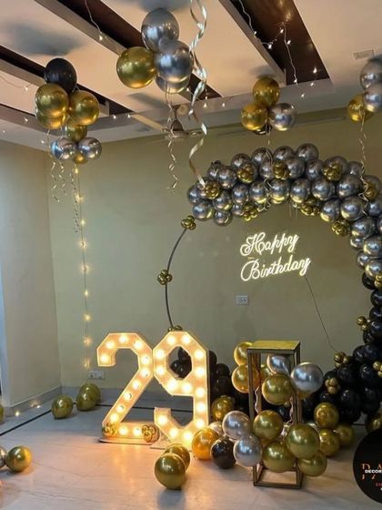 A complete room setup for a 29th birthday, featuring a black and gold balloon ring, marquee numbers, and hanging fairy lights.