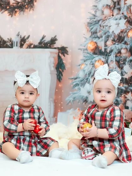A classic portrait of twin baby girls during their first Christmas photoshoot. Matching outfits and big white bows complete this adorable holiday look.