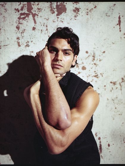 An archival shot from a menswear editorial, captured on Kodak Portra film. The image has a raw, textured quality, with dramatic lighting highlighting the model's pose and expression.