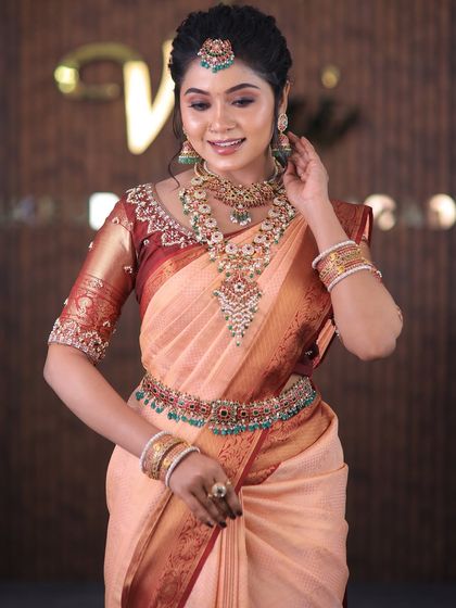 A full set from a photoshoot featuring a lovely peach-colored silk saree. The drape is kept simple and elegant to highlight the beautiful color and the intricate temple jewellery.