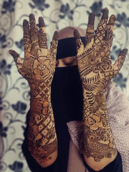 A client wearing a niqab showcases her Dubai-style mehendi. One hand features a classic jaal pattern, while the other has a bold, flowing floral design, showing how we can mix and match styles.