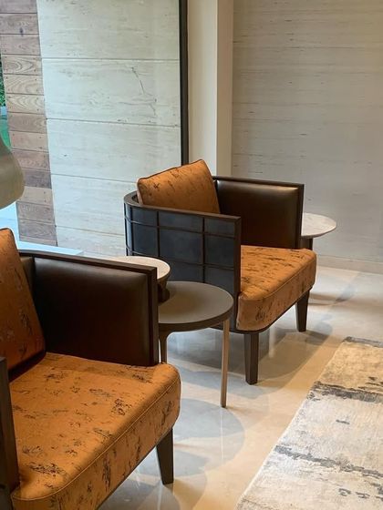 A pair of armchairs in a rich rust color provides a warm accent in the cool-toned living room. A sculpture is visible through the window, highlighting the connection between the interior and the art-filled garden.