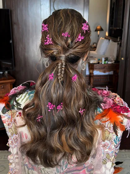 A soft and romantic low ponytail adorned with delicate pink flowers. This look is perfect for a daytime event or a whimsical bridal style.