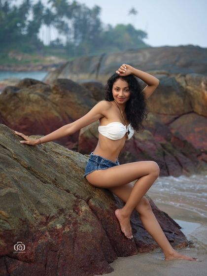 A beautiful portrait of a model sitting on the rocks by the sea. The composition and lighting create a sense of connection with the natural environment.