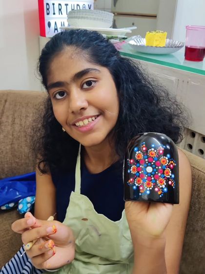 The birthday girl, Amaira, smiling as she holds up her beautifully finished dot mandala mug.