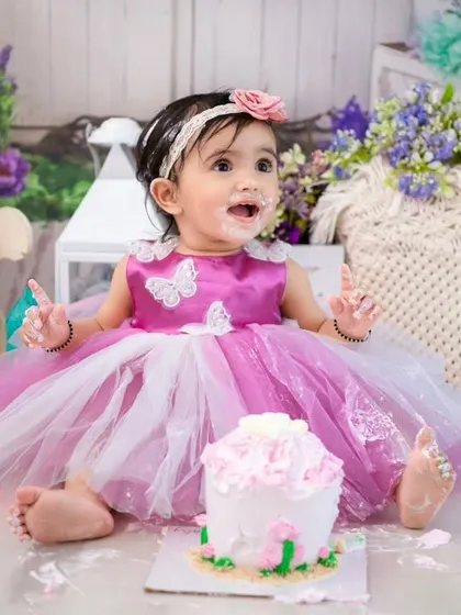A princess in pink enjoying her first birthday cake. The frosting on her hands and face is a testament to a fun and successful cake smash.