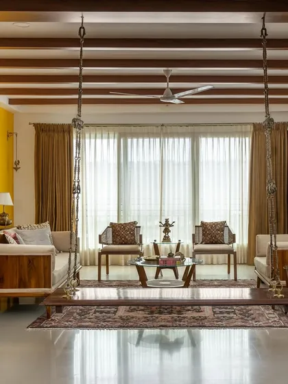 A frontal view of the 'Vasudhalayah' living room, showcasing the symmetrical arrangement of custom seating around the traditional wooden swing.