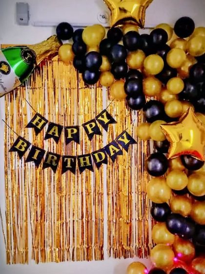 A simple and classy backdrop with a gold fringe curtain and a black and gold balloon arch.