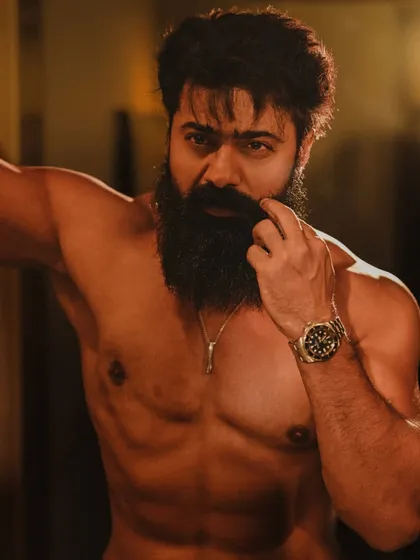 A warm, low-light portrait of Dev. The golden tones and his thoughtful expression create an intimate and moody atmosphere, highlighting his physique in a subtle way.