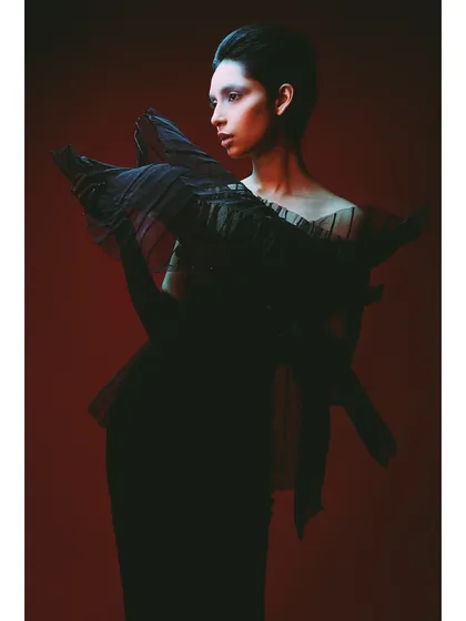 A shot from the 'Athena' series featuring a sculptural black dress against a fiery red background. The styling is avant-garde, and the lighting from the side carves out the model's silhouette.