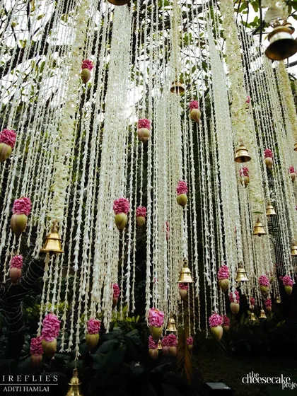 A stunning close-up of the thousands of fragrant rajnigandha strings and brass bells hanging from the champa tree, creating a magical floral curtain for the mandap.