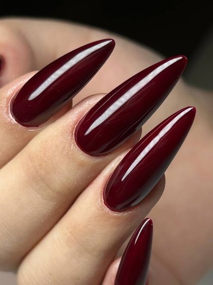 A dramatic, deep burgundy polish on long, stiletto-shaped nails. This combination of color and shape is bold, powerful, and glamorous.