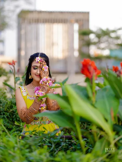 A creative portrait of the bride peeking through the flowers. This playful shot highlights her intricate henna and floral jewelry.