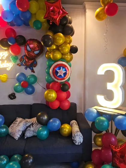 A detailed shot of the superhero birthday setup, focusing on the light-up number, Captain America's shield balloon, and the Spider-Man character.