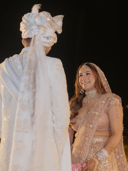 The first look. The bride's soft, romantic makeup and pastel lehenga create a breathtaking vision, perfectly captured in this moment with her groom against the evening sky.