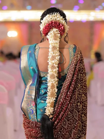 A close-up of a traditional South Indian bridal hairstyle. The long braid is intricately decorated with fresh jasmine flowers (gajra) and hair jewels, creating a classic and elegant look.