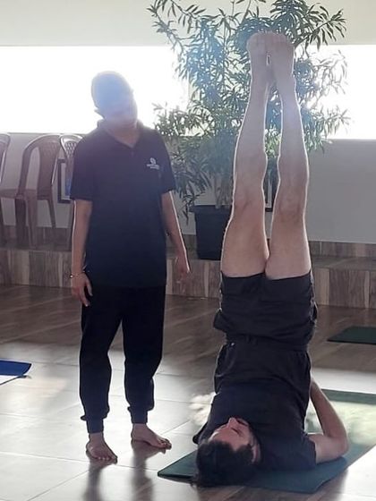 An instructor provides a hands-on adjustment to a guest in Sarvangasana (Shoulder Stand). Personalized attention is a key part of our teaching philosophy to ensure safety and proper form.
