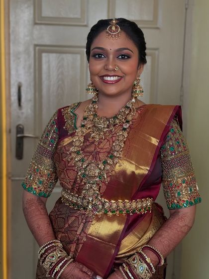 My beautiful bride Prithivi ready for her wedding ceremony in Trichy. She is wearing a traditional maroon Kanjeevaram saree with heavy antique gold jewellery, and her makeup features a bold eye and a radiant smile.